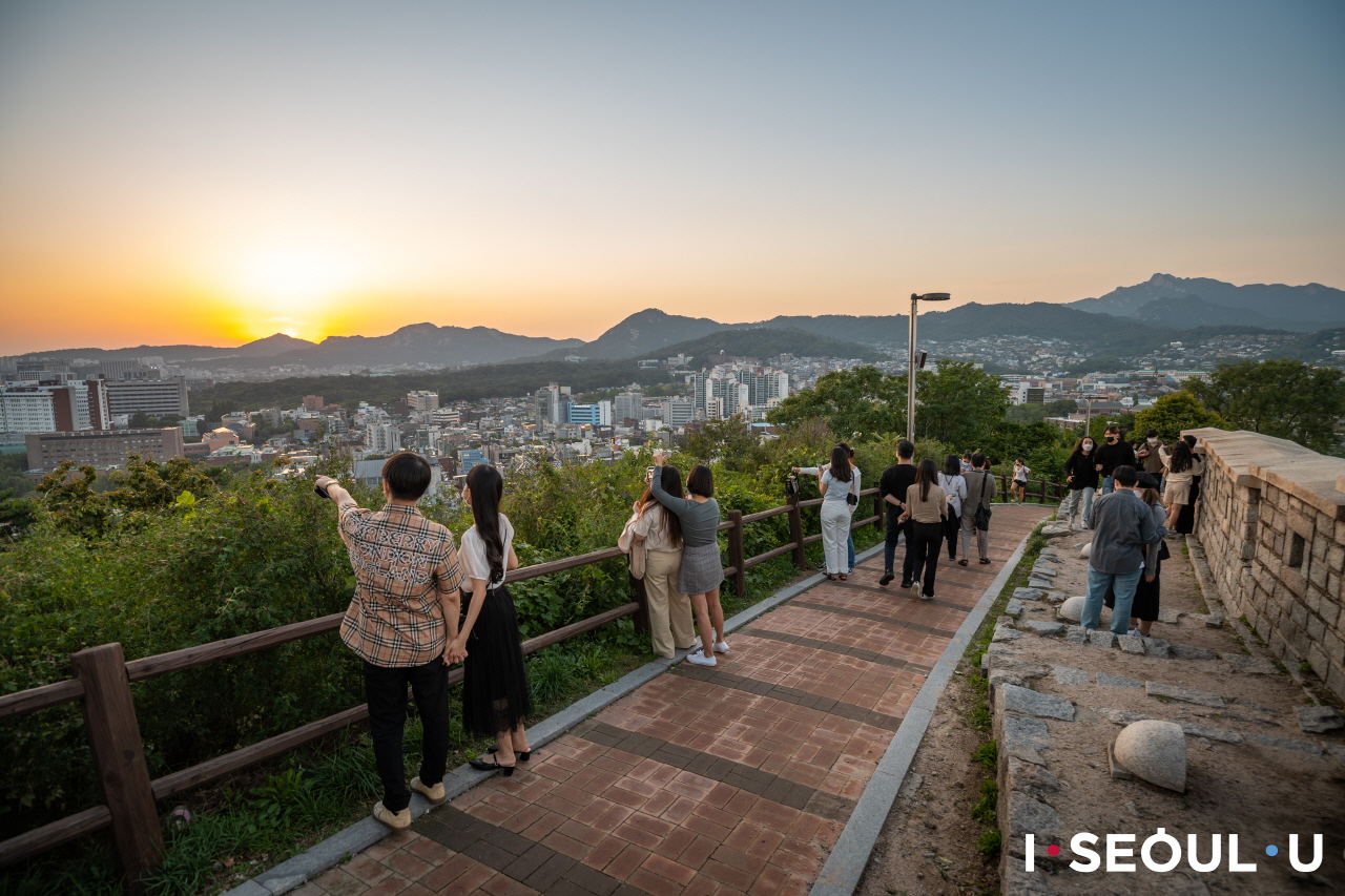 ナクサン(駱山)公園の頂上にのぼり、夕焼けに染まるソウルの都心を眺める人々